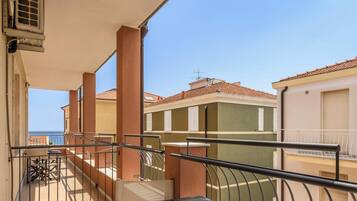A balcony with a metal railing, a view of neighboring buildings, and a clear sky.