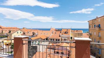 A residential area with terracotta-roofed buildings, a clear blue sky, and a view of the sea.