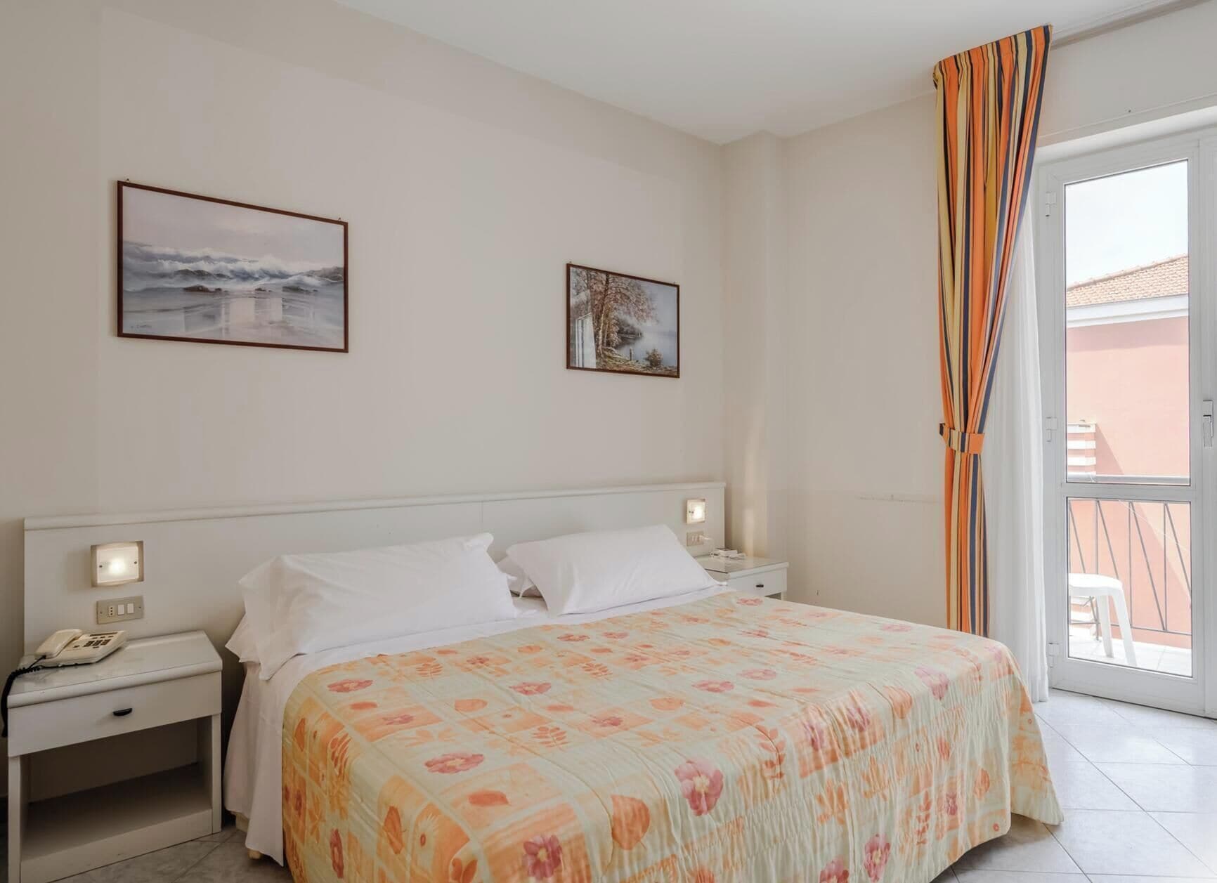 A hotel room with a bed, two bedside tables, a telephone, and a window with curtains.