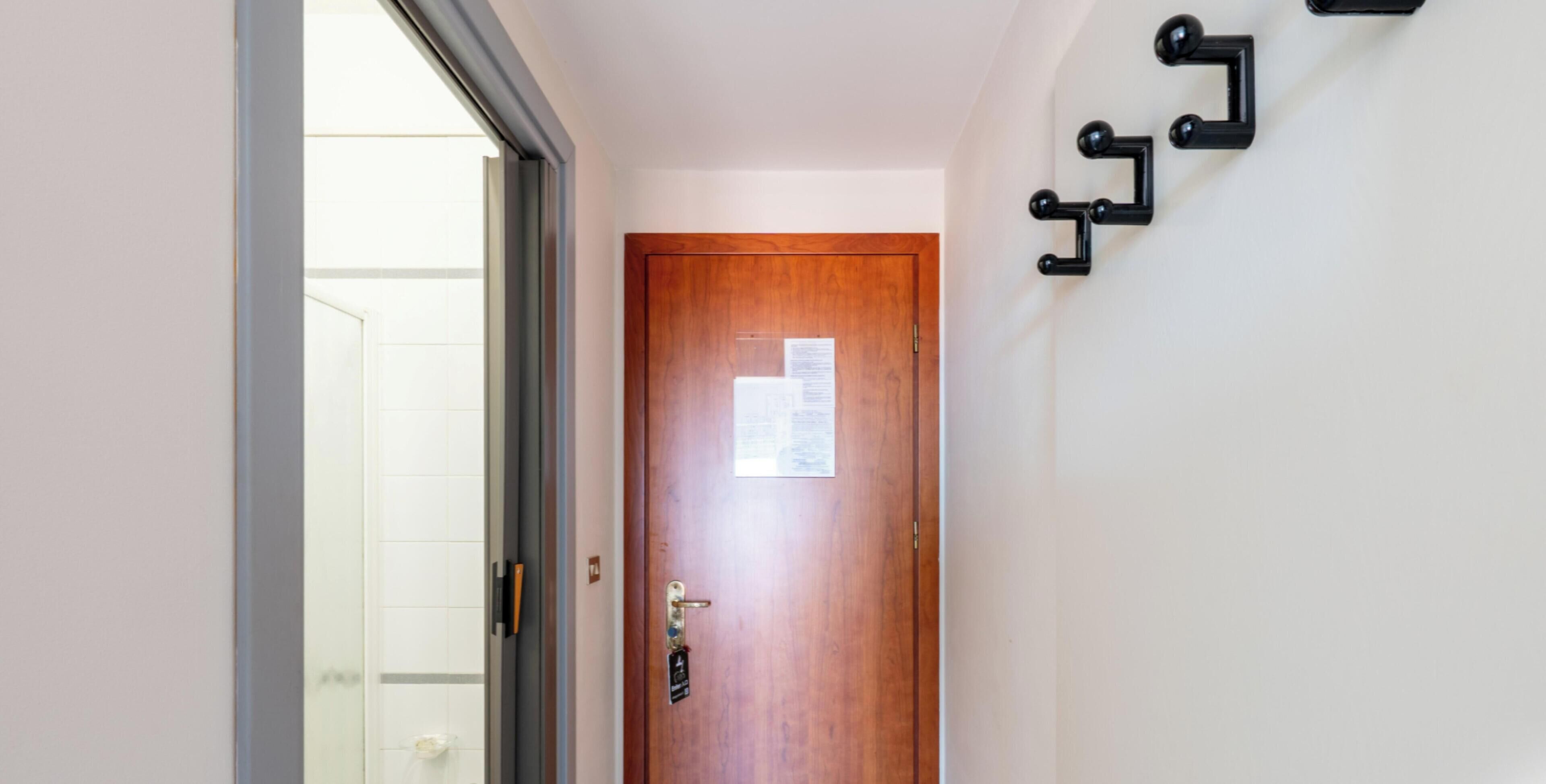 A wooden door with a keyhole and a lock, a small sign on the door, and a wall-mounted black pipe fixture.