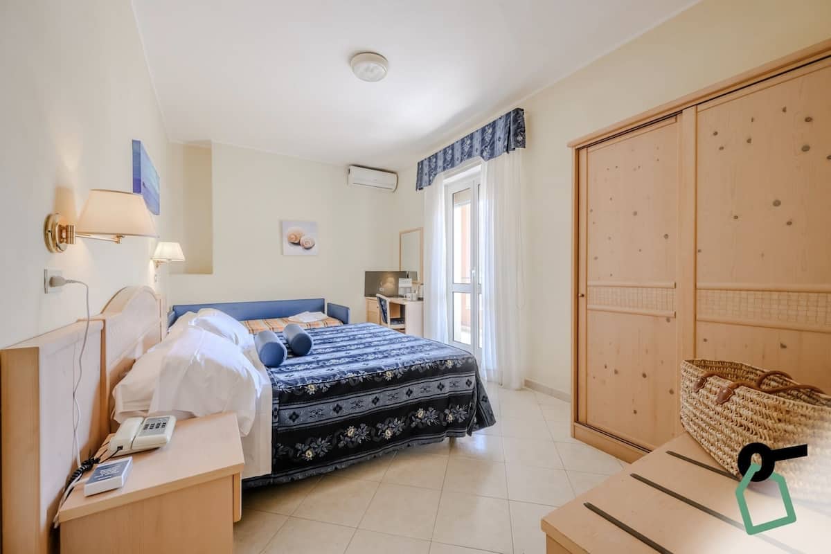 A hotel room with a bed, bedside table, lamp, desk, and wardrobe.