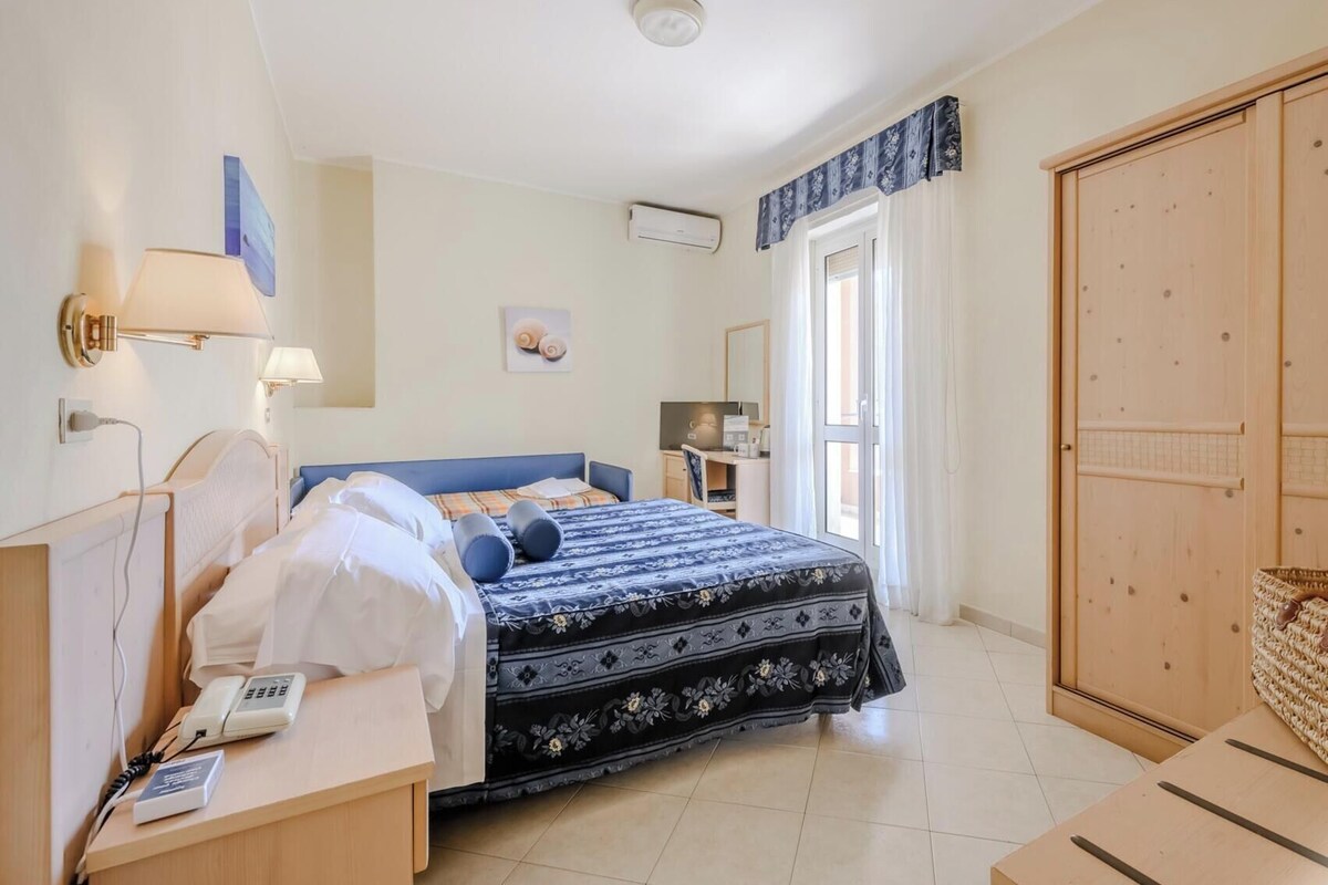 A hotel room with a bed, bedside table, lamp, desk, and wardrobe.