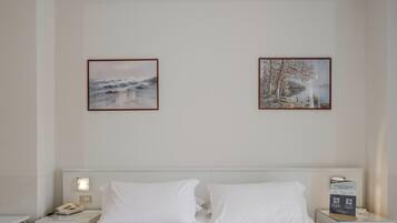 A hotel room with a bed, two framed pictures on the wall, a bedside table with a lamp, and a nightstand with a phone.