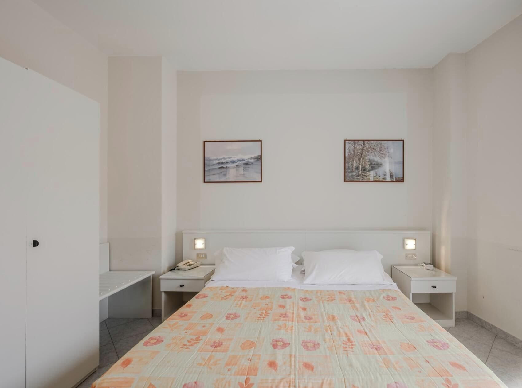 A bedroom with a bed, two bedside tables, and two wall-mounted light switches.