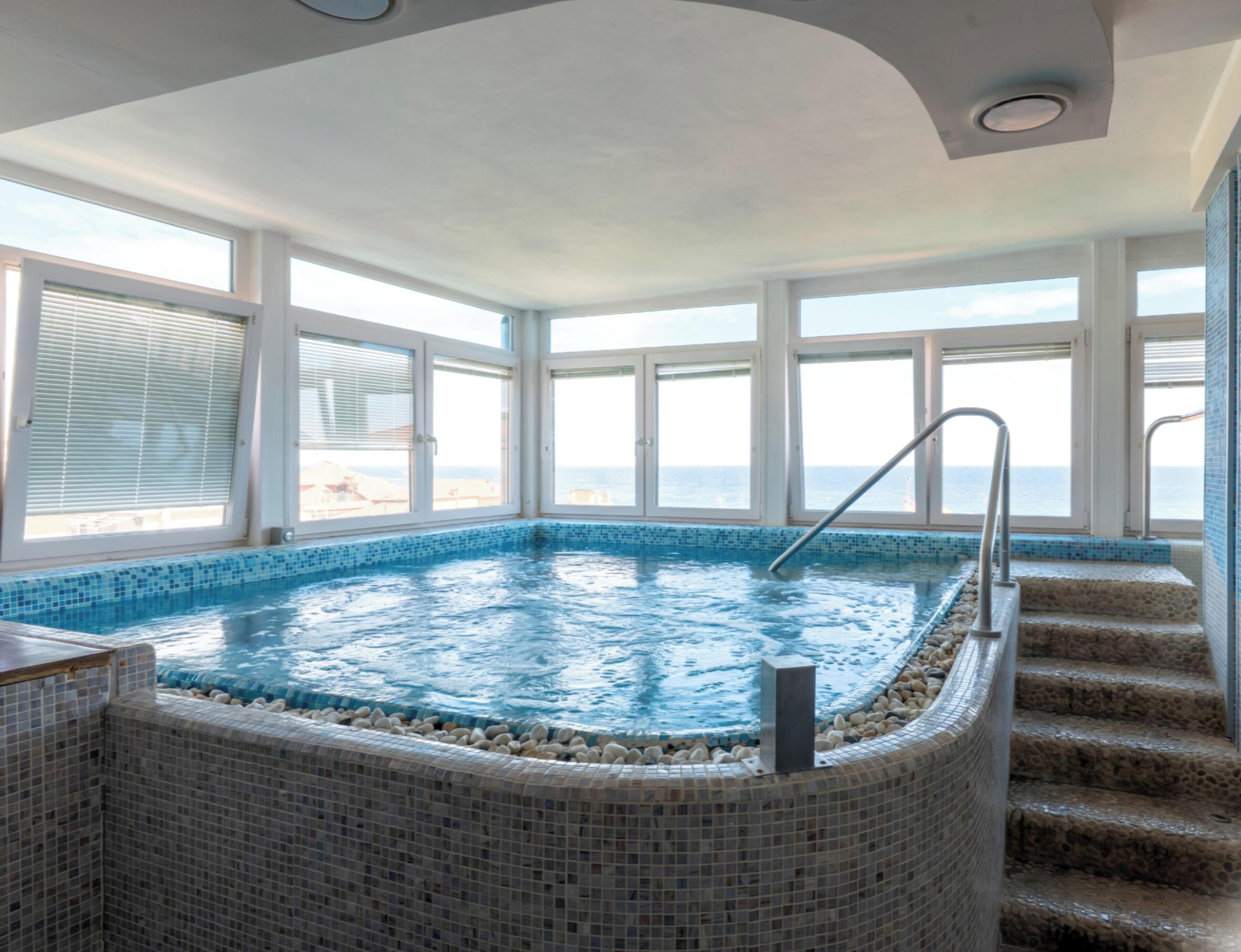A large indoor swimming pool with a view of the sea through large windows.
