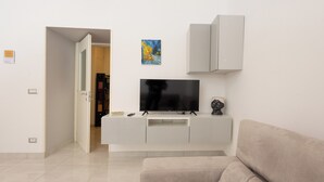 A modern living room with a flat-screen TV on a white entertainment unit, a beige sofa, and a door leading to another room. - Civico 79 - Two Bedroom Apartment, Sleeps 4 (Naples)