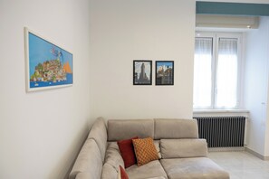 Un salón con un sofá color beige, dos cuadros en la pared y un radiador.