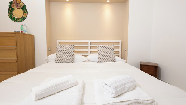 A neatly made bed with two pillows, a wooden dresser, and a small bedside table. - Civico 79 - Two Bedroom Apartment, Sleeps 4 (Naples)