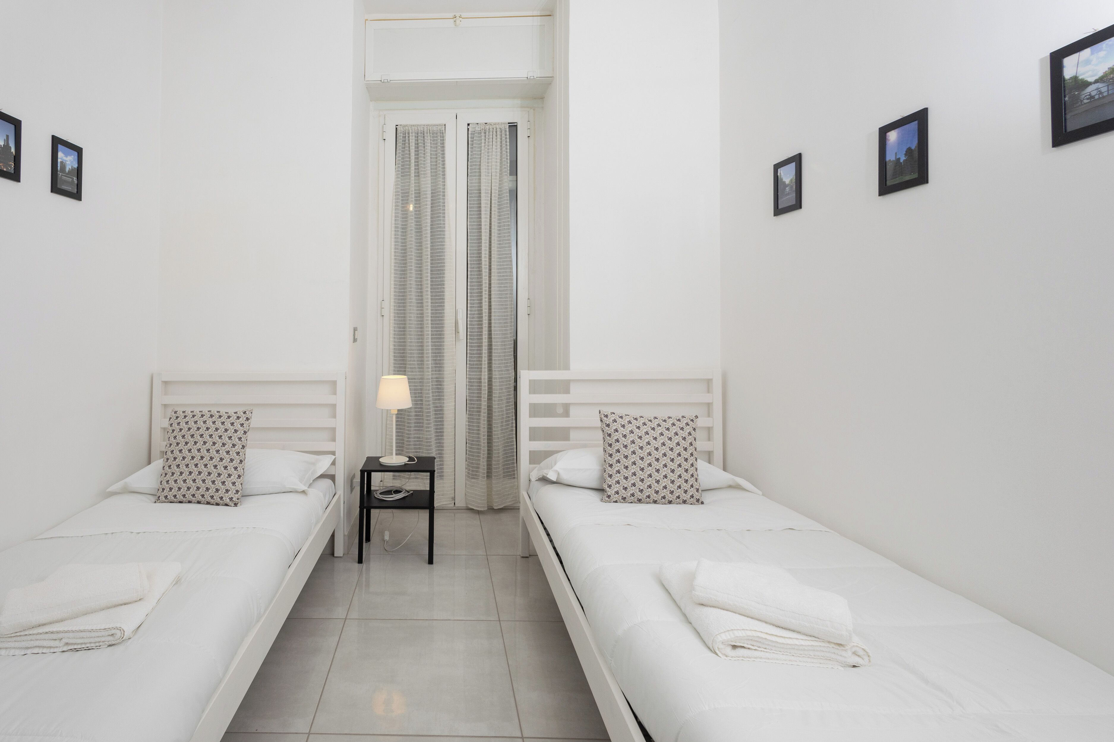 Habitación doble con dos camas individuales, una mesita de noche con lámpara y ventana con cortinas.