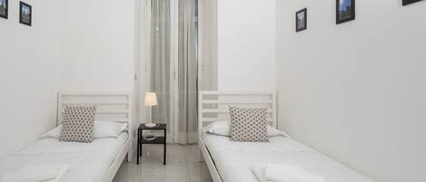 Habitación doble con dos camas individuales, una mesita de noche con lámpara y ventana con cortinas.