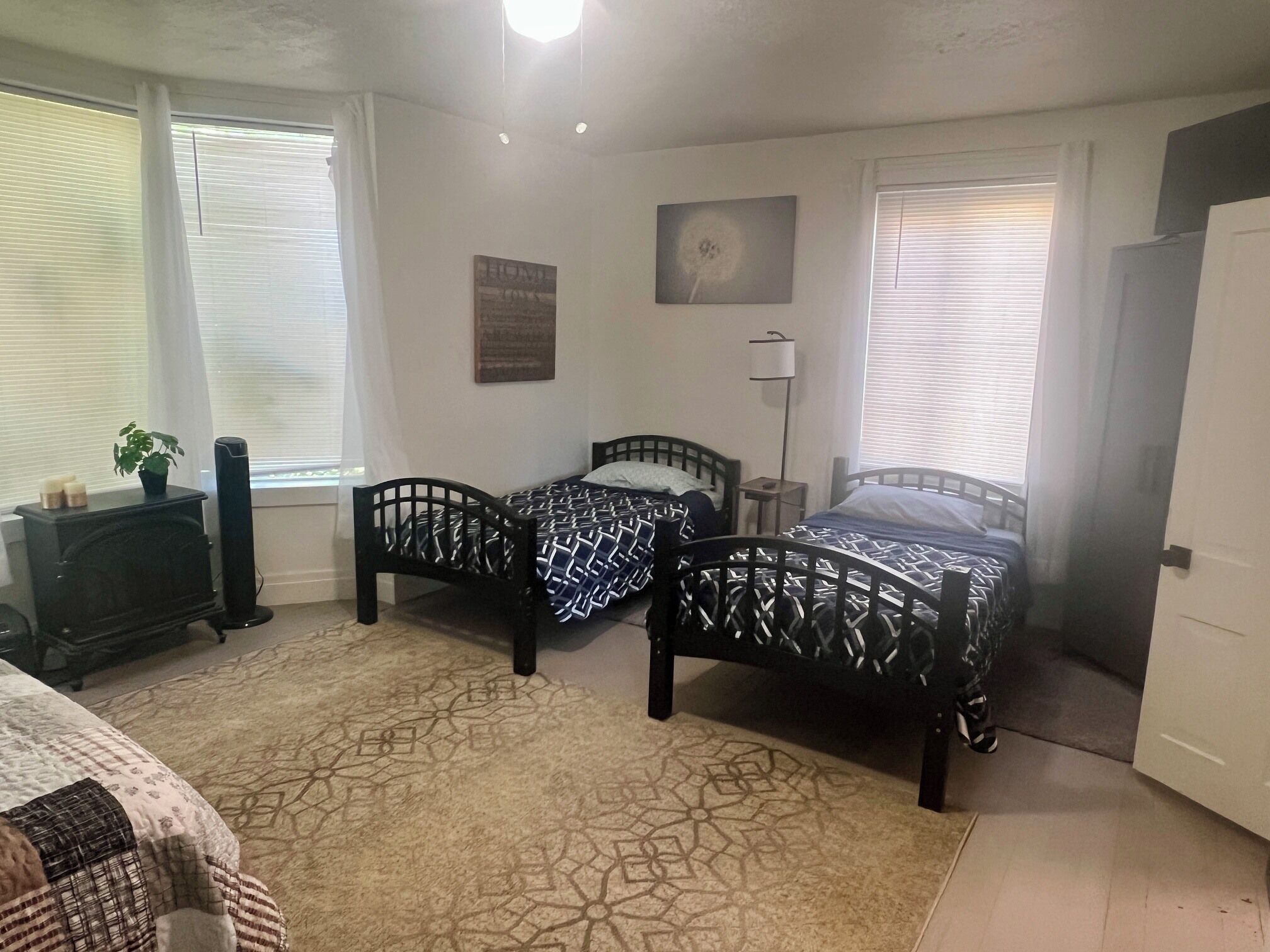 A bedroom with two beds, a heater, a plant, and a window with blinds.