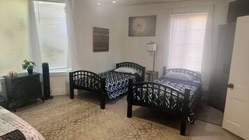 A bedroom with two beds, a heater, a plant, and a window with blinds.
