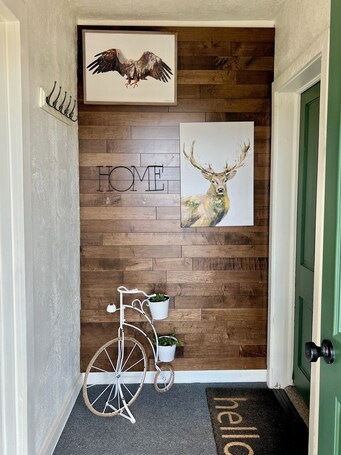 A wooden wall with a 'HOME' sign and a deer painting. There is a white metal bike rack with potted plants.