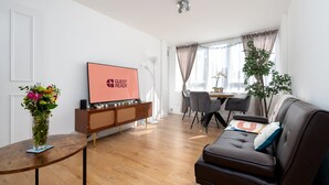 Un soggiorno moderno con una TV a schermo piatto, un'area pranzo con tavolo e sedie, e un divano con cuscini decorativi.