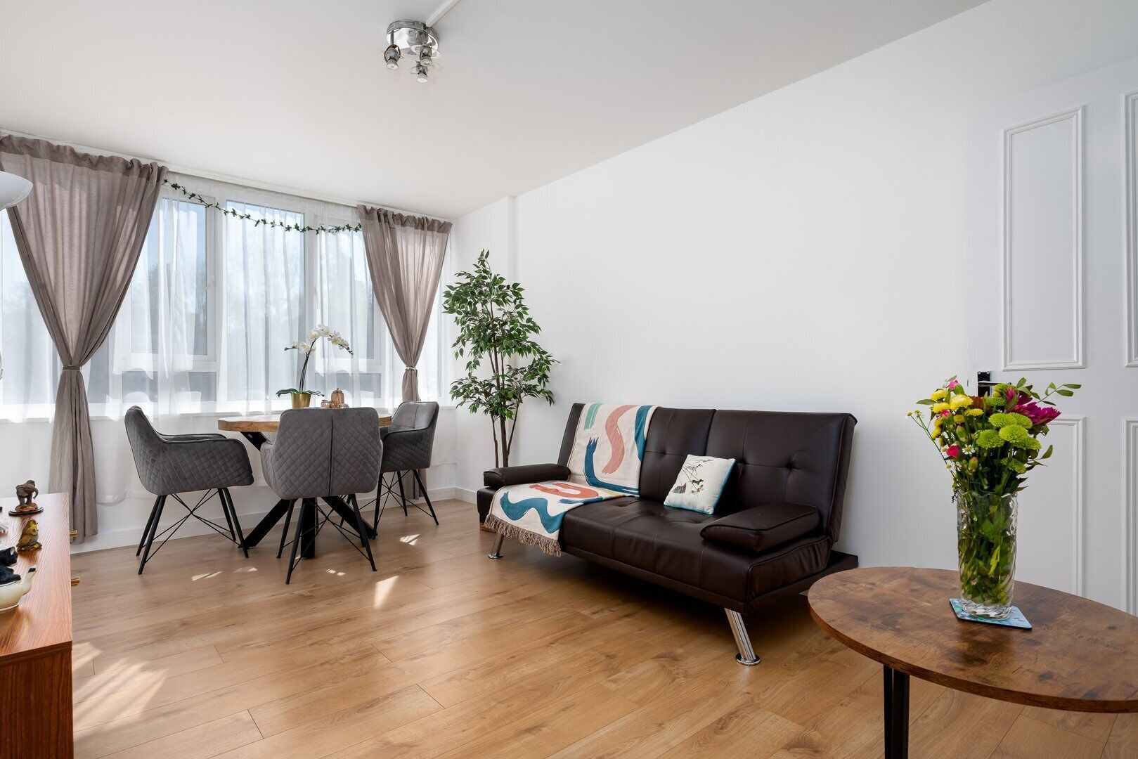 Een moderne woonkamer met een bruine leren bank, een houten salontafel en een eethoek met een tafel en stoelen.