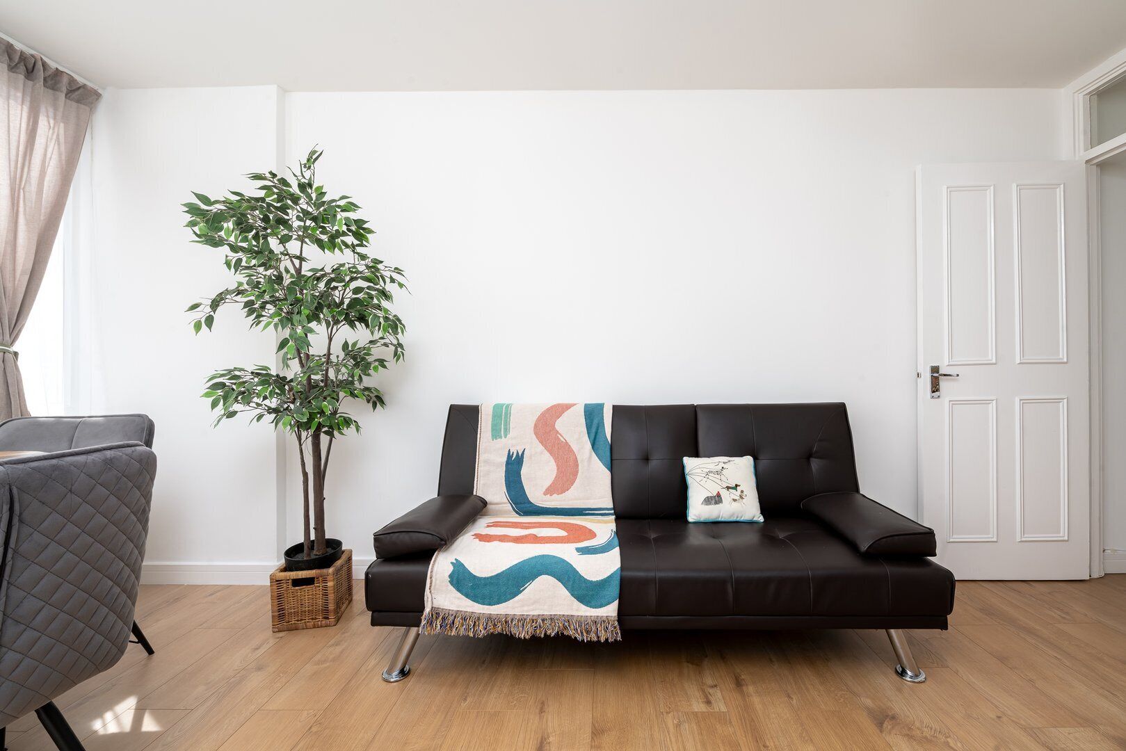 A modern living room with a black leather sofa, a potted plant, and a colorful throw blanket.