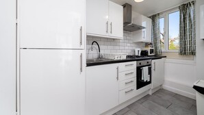 Una cucina moderna con mobili bianchi, un piano di lavoro nero, un fornello e una finestra con tende.