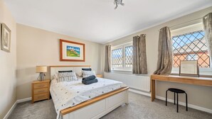 A bedroom with a bed, bedside table, lamp, window with curtains, radiator, and a desk with a chair. - Spacious and pet-friendly stay near New Forest (Totton)