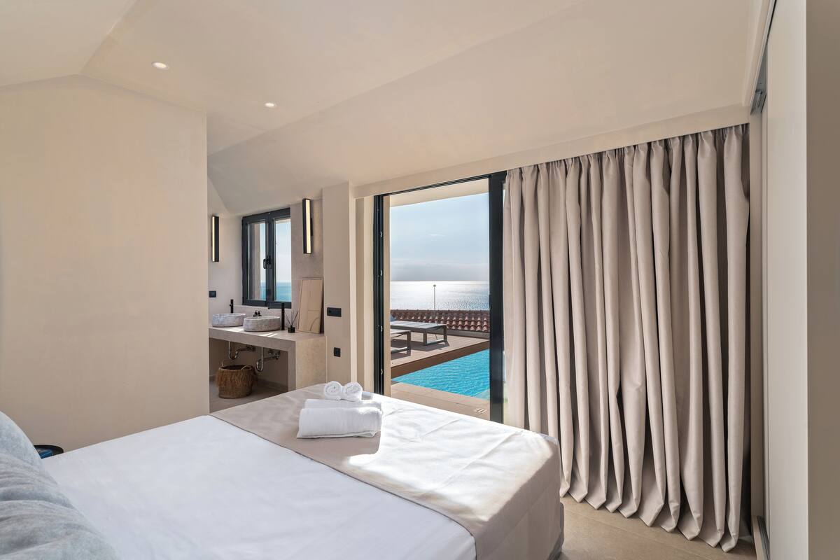 A hotel room with a bed, a bathroom with a sink, and a view of a pool and ocean.