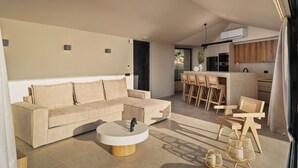 Un salon moderne avec un canapé beige, une table basse ronde et un coin repas comprenant des chaises en bois, avec une cuisine en arrière-plan.