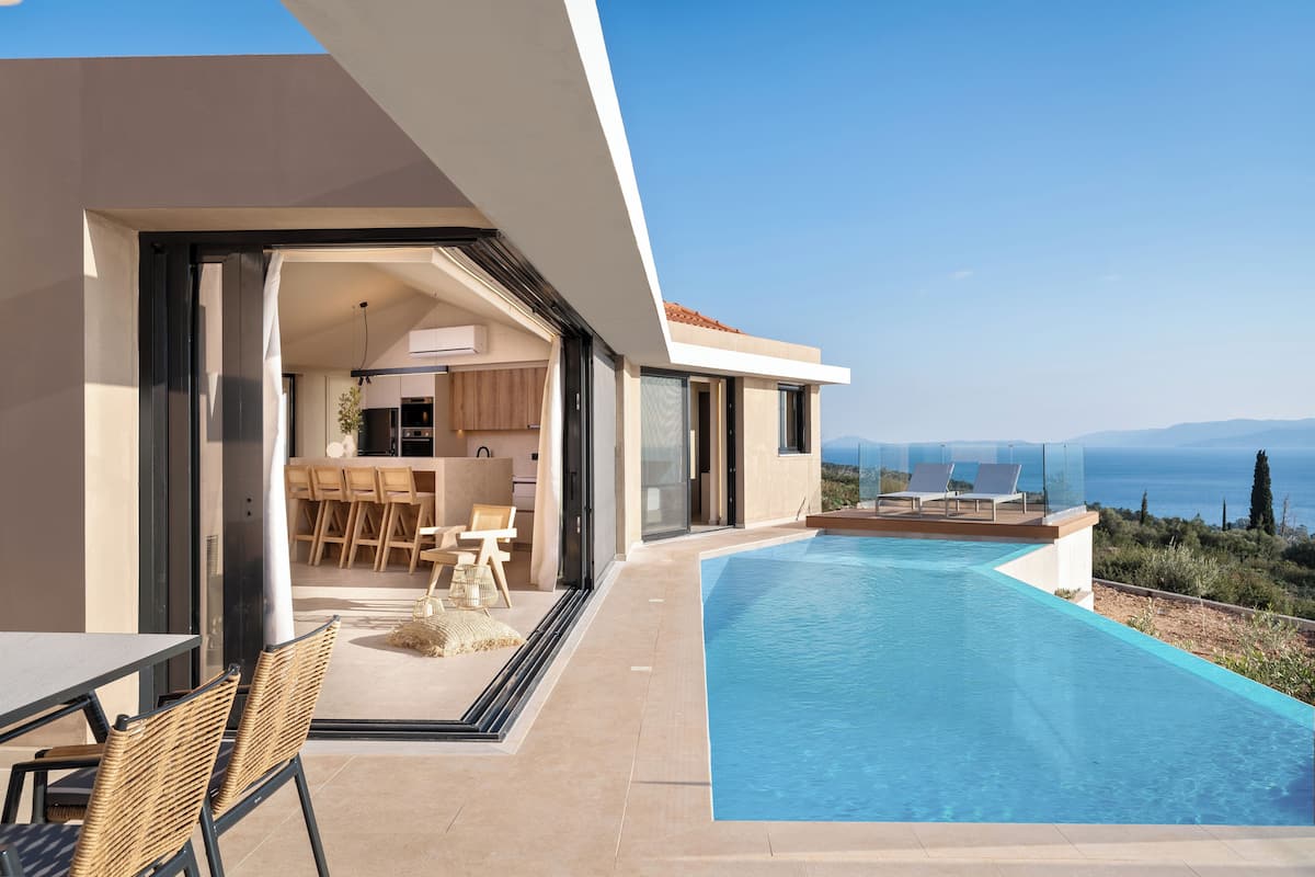 A modern house with a swimming pool, a dining area, and a view of the sea.