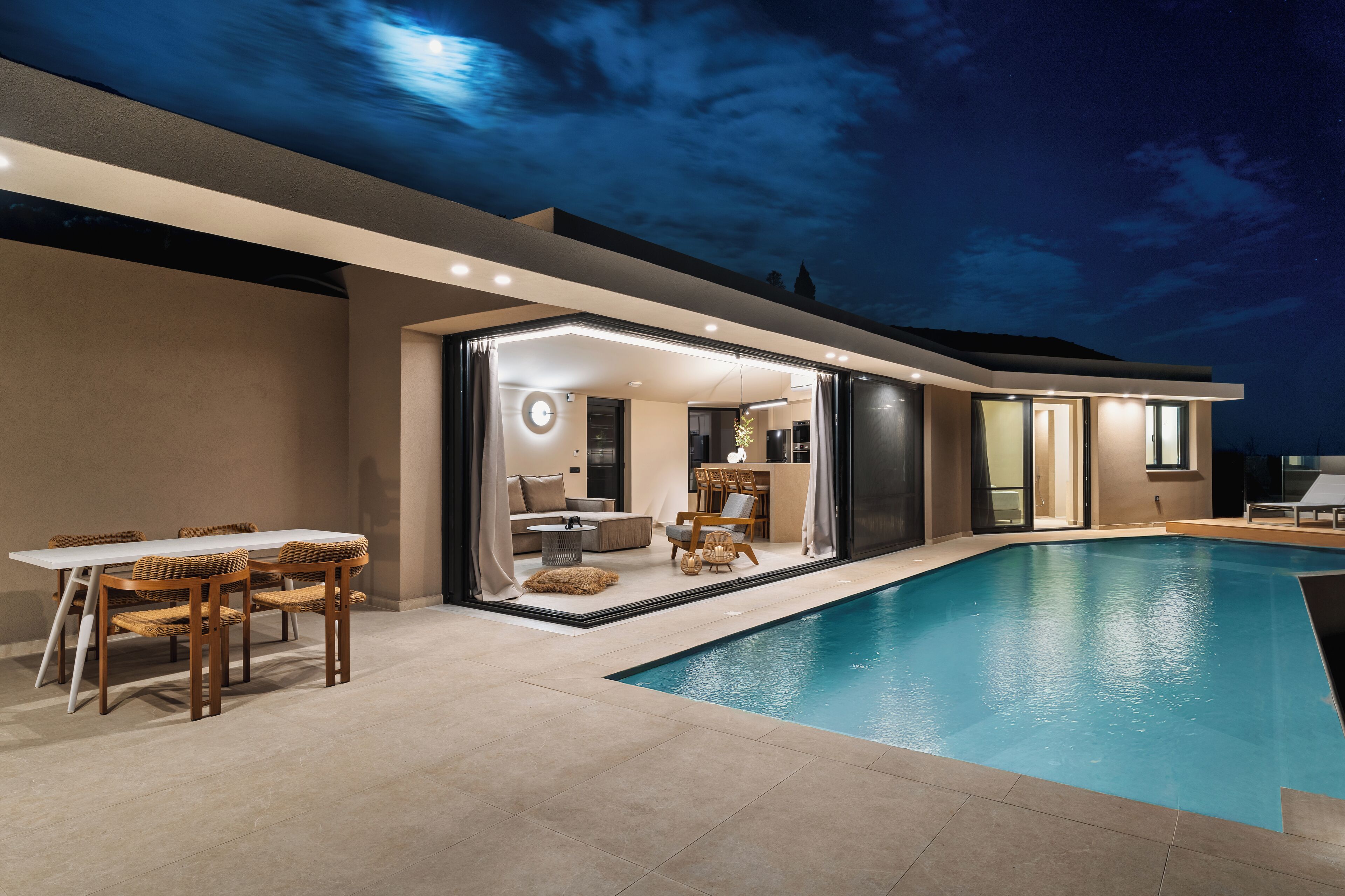 Una casa moderna con piscina, un comedor con sillas de mimbre e interiores bien iluminados.