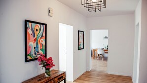 Un corridoio con pavimento in legno, un consolle di legno con un vaso di fiori e due quadri astratti appesi alle pareti.