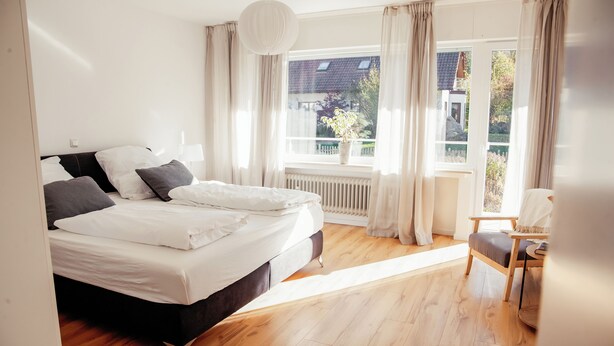 Una camera da letto con un letto grande, una sedia, una finestra con tende e un termosifone.
