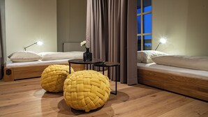 A modern bedroom with two beds, a small table, and two woven ottomans.