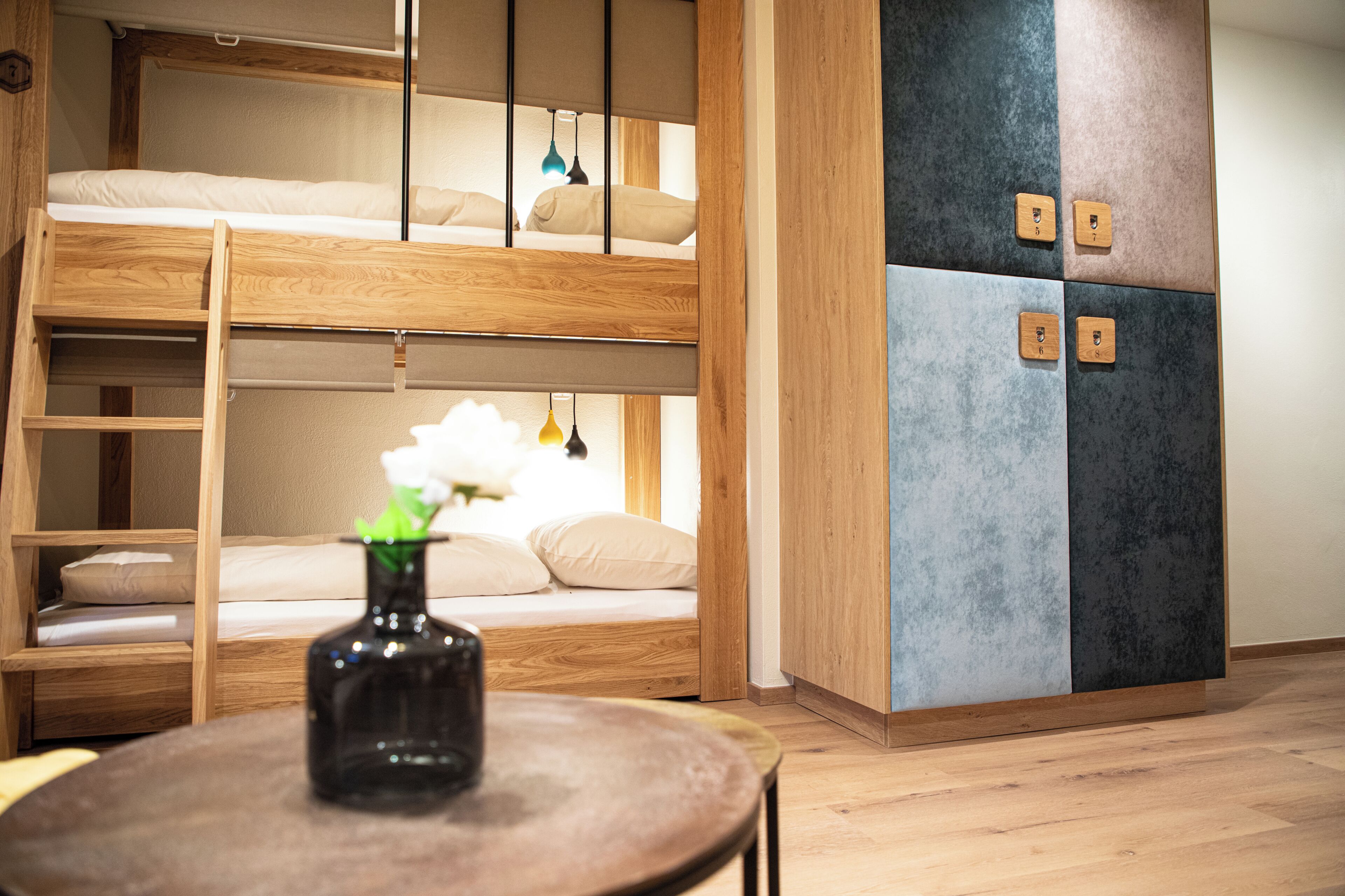 A bunk bed room with a wooden wardrobe and a small table with a vase.