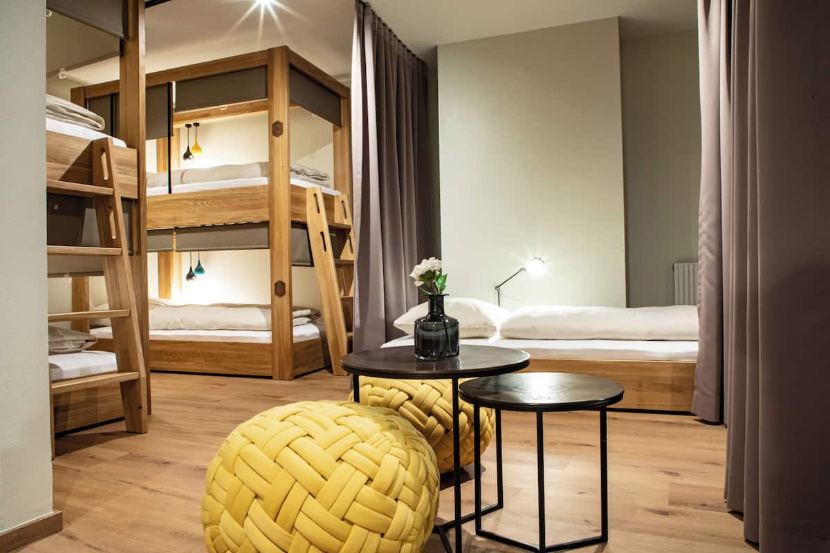 Ein Zimmer mit Etagenbetten, einem runden gewebten Hocker, einem kleinen Tisch und einer Pflanze in einer Vase.