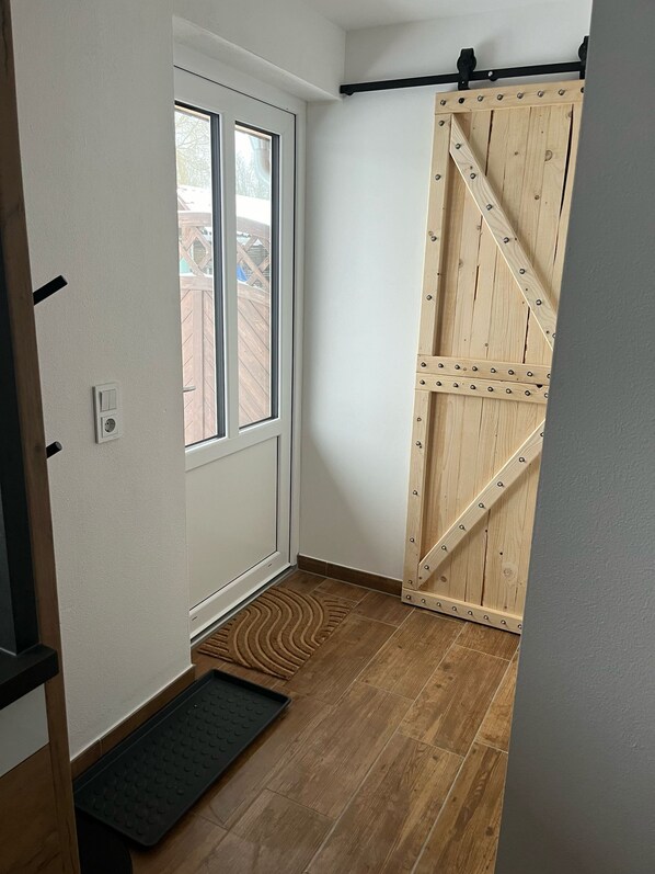 Una habitación con una puerta corredera de madera, una ventana y un felpudo negro en la entrada.