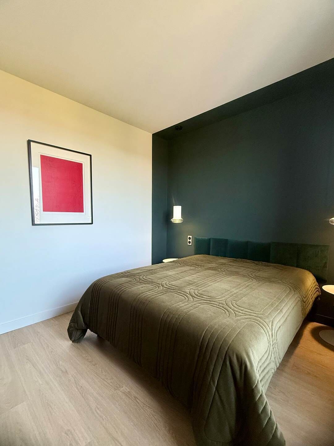 Quarto moderno com uma cama grande, uma obra de arte emoldurada na parede e uma mesa de cabeceira com abajur.