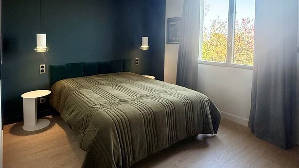 A bedroom with a bed, two bedside tables, a window with curtains, and a view of trees outside. - MALACHITE (double room) (Carcassonne)