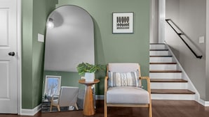 A modern interior with a green wall, a large mirror, a wooden chair, and a staircase. - Walk to downtown St. Charles: Hot Tub, 4K TV Surround Sound, Espresso, Fire pit! (St. Charles)