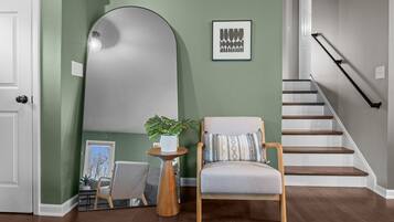 A modern interior with a green wall, a large mirror, a wooden chair, and a staircase.
