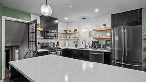 A modern kitchen with a large island, stainless steel appliances, and open shelving with plants. - Walk to downtown St. Charles: Hot Tub, 4K TV Surround Sound, Espresso, Fire pit! (St. Charles)
