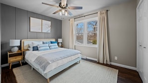 A bedroom with a bed, nightstands, a ceiling fan, a window with curtains, and a door. - Walk to downtown St. Charles: Hot Tub, 4K TV Surround Sound, Espresso, Fire pit! (St. Charles)