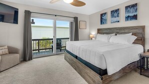 A bedroom with a large bed, a ceiling fan, a balcony with a chair, and artwork on the walls. - Seahorse Siesta (Pensacola Beach)