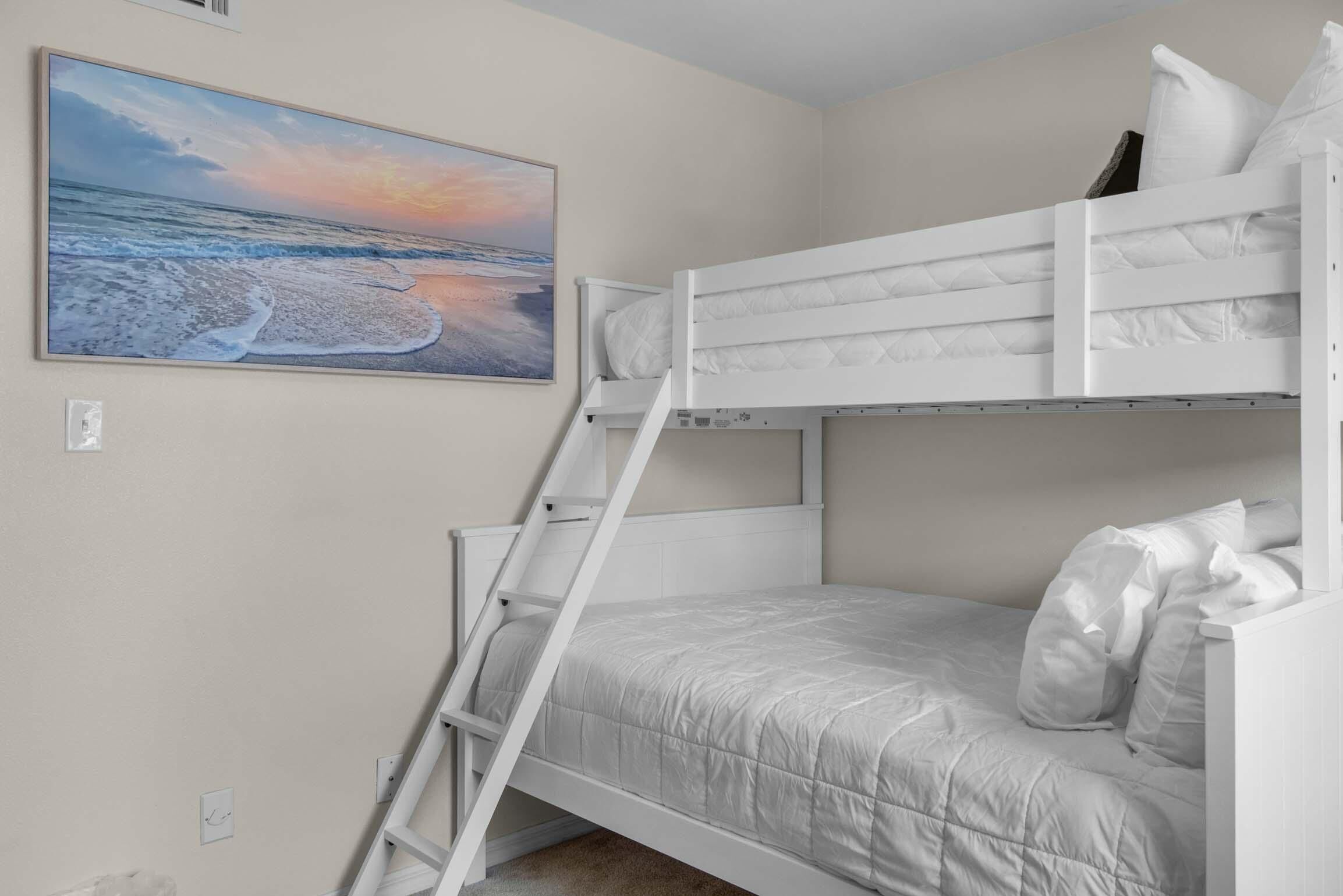 A bunk bed room with a ladder, a painting of a beach, and a white wall.