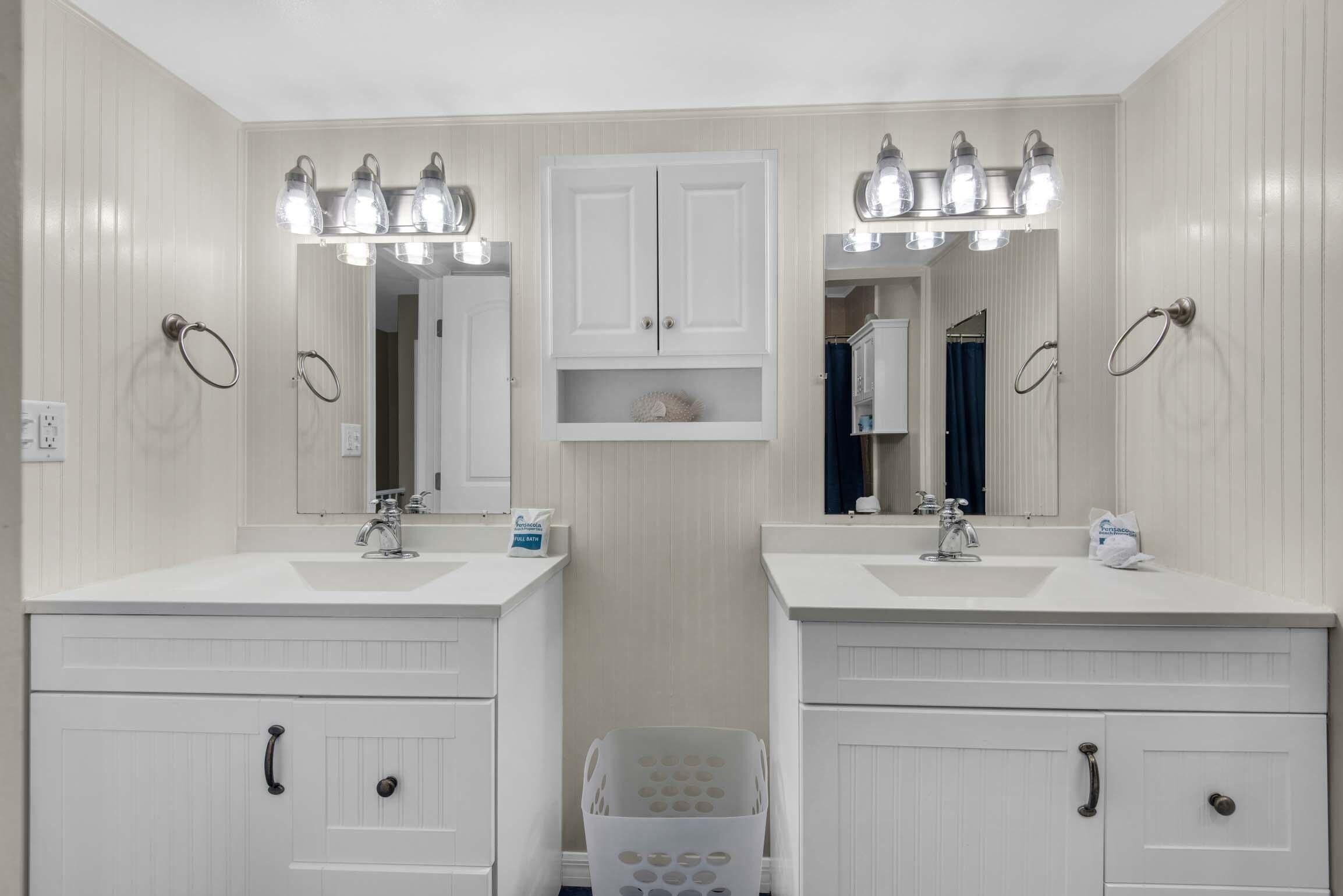 Une salle de bain avec deux lavabos, un miroir et un panier à linge.