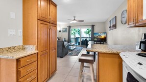 A kitchen with wooden cabinets, a granite countertop, a built-in oven, and a dining area with a view of the outdoors. - Seahorse Siesta (Pensacola Beach)
