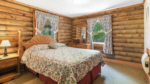 A log cabin bedroom with a wooden bed, a nightstand, a dresser, and two windows with floral curtains. -  Carters Lakeside Log Cabin #1. Located in Carters Lake Marina, with boat slip ! (Chatsworth)