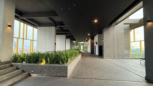 Un pasillo interior moderno con ventanas amplias, una zona central con plantas y una escalera que sube a un nivel superior.