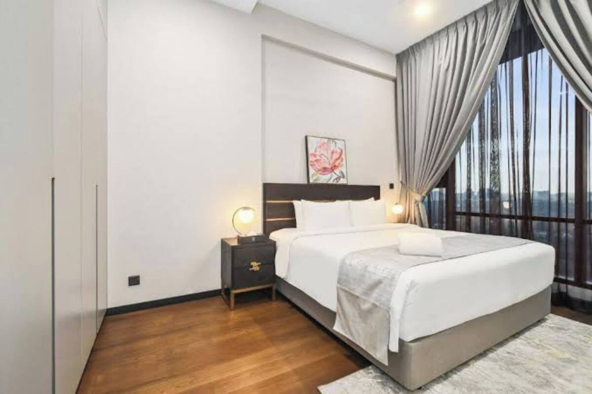 A modern bedroom with a large bed, a nightstand with a lamp, and a window with curtains.