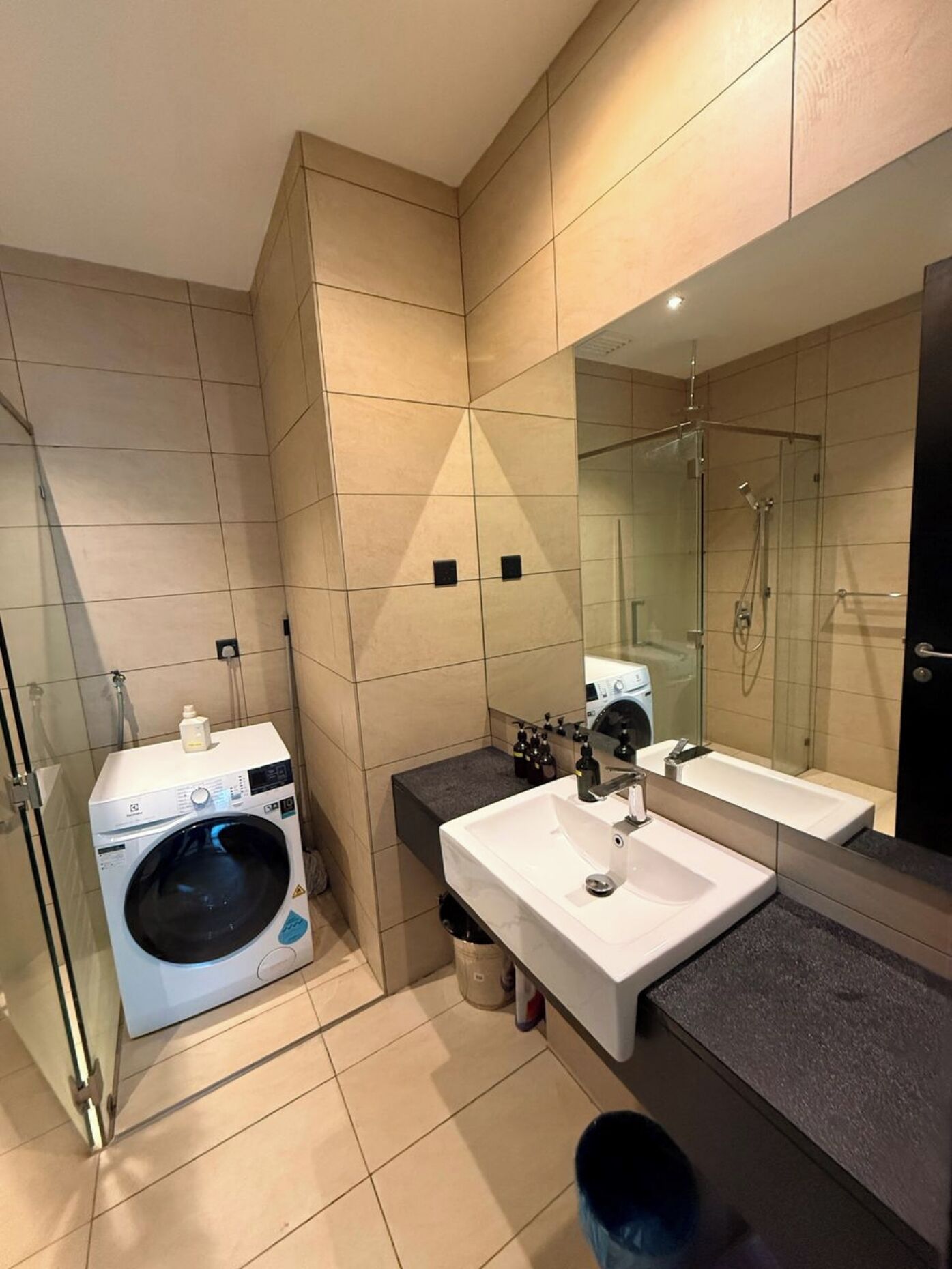 A modern bathroom with a washing machine, a sink, and a glass-enclosed shower.