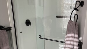 A glass-enclosed shower with a towel rack and a patterned mat at the entrance. - Historical B&B located in New York's Finger Lakes Region (Seneca Falls)