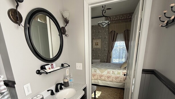 A bathroom with a large mirror, dark wooden cabinets, a white sink, and a shower area. - Historical B&B located in New York's Finger Lakes Region (Seneca Falls)