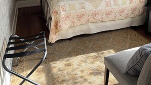 A bedroom with floral wallpaper, a bed with a patterned bedspread, a chair, a bedside table, and a window with curtains. - Historical B&B located in New York's Finger Lakes Region (Seneca Falls)