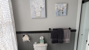 A bathroom with a toilet, a sink, and two wall-mounted paintings. - Historical B&B located in New York's Finger Lakes Region (Seneca Falls)
